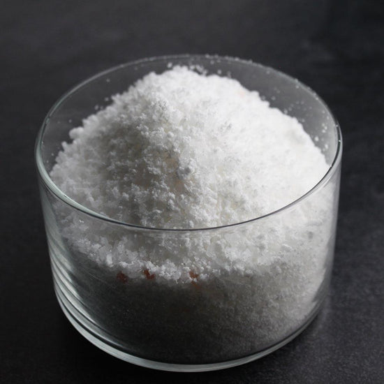 Close-up of a clear glass bowl filled with white granular Mermaid Bubbling Bath Salts | Primal Elements, highlighting the texture for wellness and body care use.