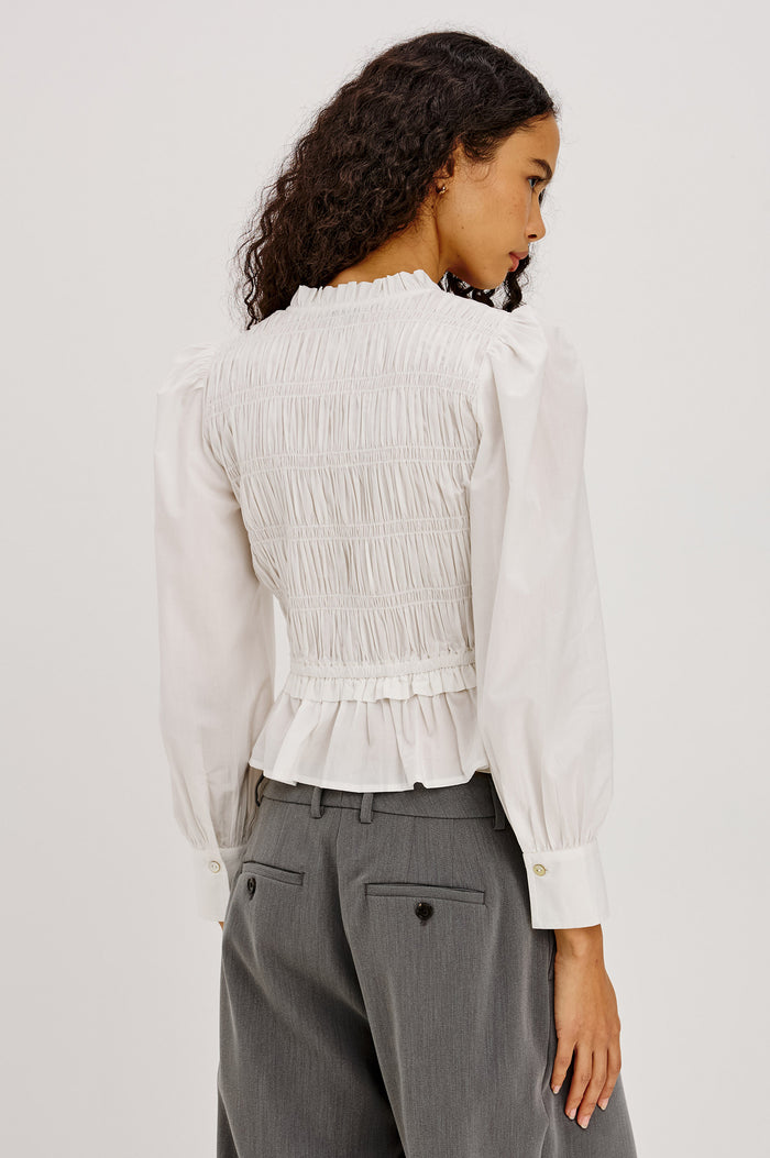 Sami Shirt in Cotton Poplin With V-Neckline Front Ties, Shirred Fitted Bodice, Flared Hem, Ruffle Trim, and Long Puff Sleeves With Buttoned Cuffs in White Colorway - Upper Body Back View Featured on Model