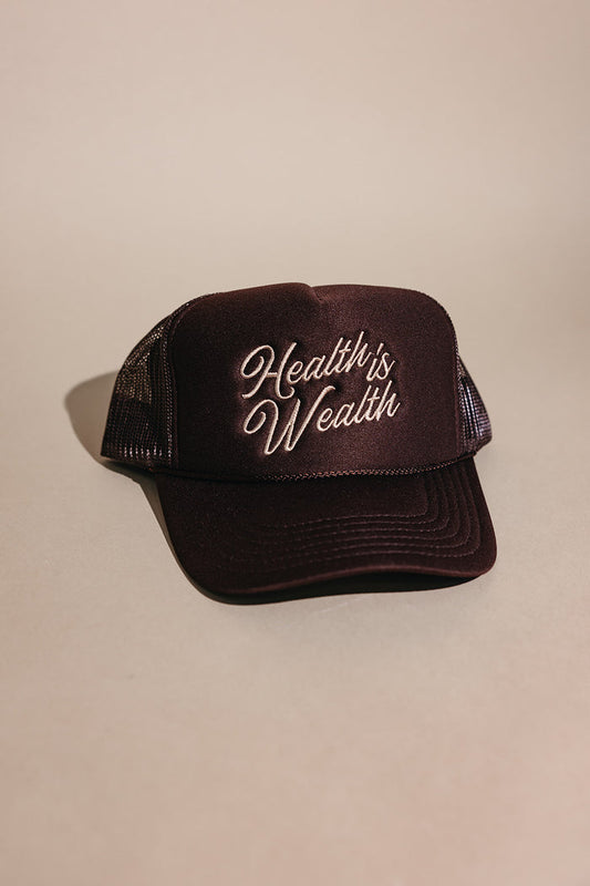 Dark brown mesh trucker hat with "Health is Wealth" embroidered in cream script on the front panel, featuring the Health is Wealth Trucker Hat | Lucky Owl design.