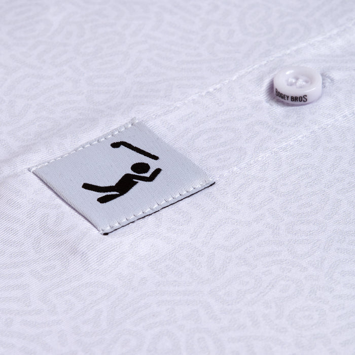 Close-up of the Stealth Mode - Light - Polo, a white athletic-fit shirt with a subtle abstract texture. The fabric tag displays a black golfer icon, and a nearby button is engraved with BOGEY BROS.