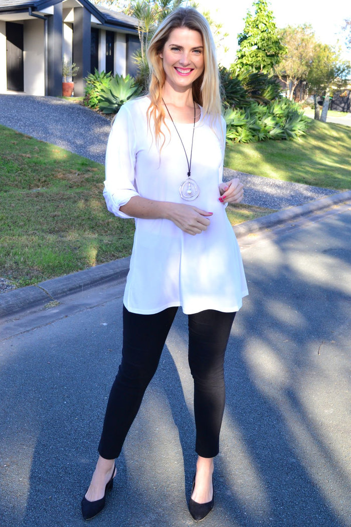 Lilia white button-up long sleeve basic tunic hanging on a hanger, showcasing its simple, classic design and clean fabric.